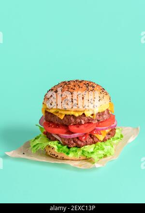 Double hamburger maison minimaliste sur fond vert. Image verticale avec un délicieux cheeseburger juteux et rempli de papier ciré. Banque D'Images