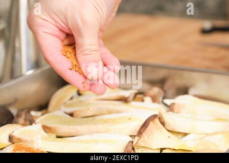 Gros plan des mains d'homme ajoutant des épices rouges sur des champignons en tranches de trompette (pleurotus eryngii), des pommes de terre et des oignons. Processus de cuisson. La Méditerranée meurt Banque D'Images