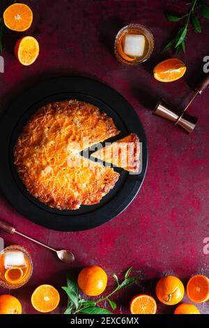 Plat encore vivant d'un gâteau à l'envers orange sur un plat de service noir entouré d'oranges, d'outils de bar et de cocktails. Banque D'Images