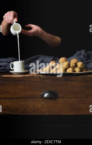 Une main tenant un pichet verse du lait dans une tasse à côté des boules de protéines Banque D'Images