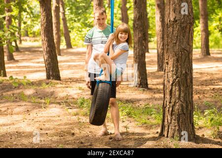 Père poussant enfant fille sur la balançoire de pneu dans la forêt d'été. Week-end familial actif. Photo de haute qualité Banque D'Images