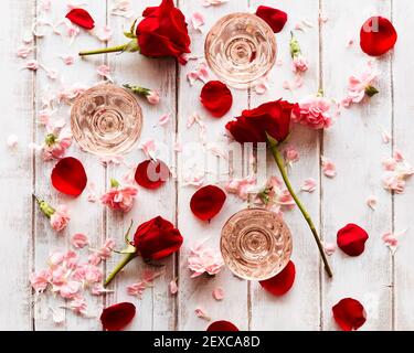 Lunettes de coupé vintage garrées de rosé sur une surface en bois blanchi à la chaux entourée de fleurs et de pétales rouges et roses. Banque D'Images