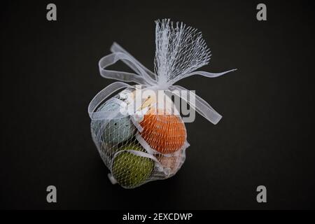 Œufs de Pâques décoratifs de couleur dans un sac en filet blanc sur le noir arrière-plan Banque D'Images