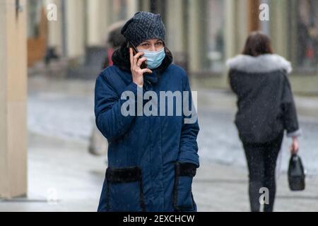 Fille ou femme marchant avec le masque et parlant sur le Téléphone dans la rue sous la pluie pendant Covid ou Urgence du coronavirus Banque D'Images