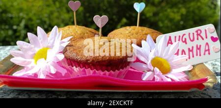 Plateau avec 3 muffins et carte de vœux de fête des mères, il y a deux pâquerettes et quelques cuiricini, la carte est écrite en italien Banque D'Images