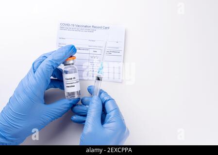 Mains gantées tenant un flacon avec le vaccin Covid-19 et la seringue, la fiche de vaccination, passeport de vaccination, sur fond blanc, gros plan, cop Banque D'Images