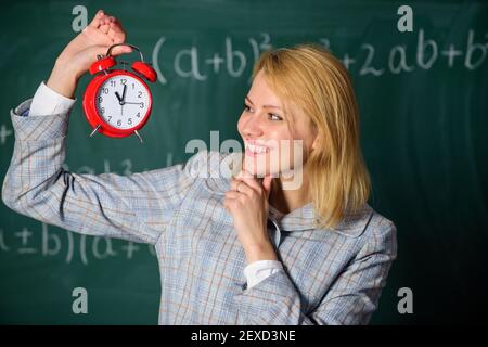 Femme enseignant tenir le réveil. Professeur d'école. Quelle heure est-il. Programme des leçons. Bienvenue à l'année scolaire des enseignants. Santé et régime quotidien. Leçon de début d'éducateur. Elle se soucie de la discipline. Banque D'Images