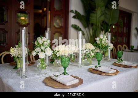 Table avec serviette et verts, assiettes en bois et verres verts, vases avec fleurs blanches et bougies Banque D'Images