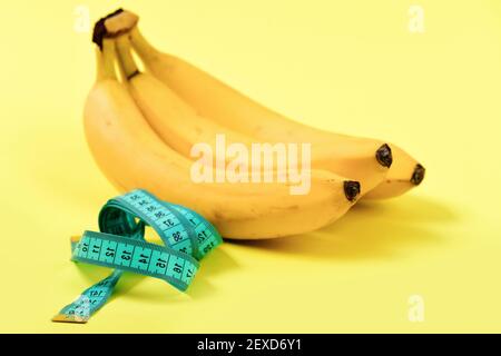 Pour la mesure de bande de couleur turquoise à côté de tas de bananes, isolé sur fond jaune clair. Concept de régime alimentaire faible en calories et vitamines alimentation Banque D'Images