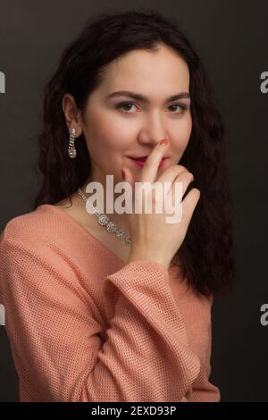 Studio portrait d'une brunette dans une robe pêche, il égratignure son nez avec ses doigts Banque D'Images