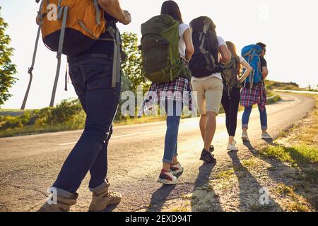 Groupe de personnes avec des sacs à dos marchant le long de la route de campagne. Les touristes randonnées dans la nature le week-end d'été Banque D'Images