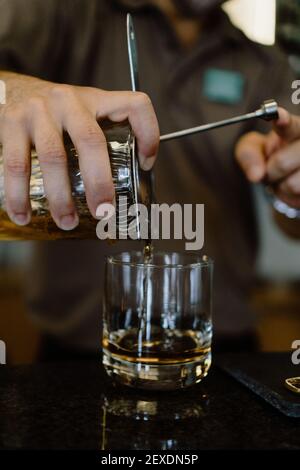 Un cliché vertical d'un barman versant le whisky dans un verre d'un récipient avec un tamis Banque D'Images