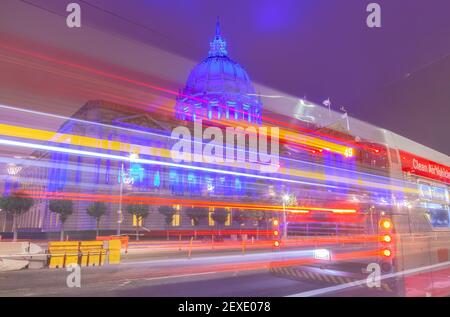 Le bus électrique passe dans la rue tandis que l'hôtel de ville de San Francisco s'allume en bleu pour rendre hommage aux travailleurs de la santé pendant la pandémie COVID-19, Californie, États-Unis. Banque D'Images