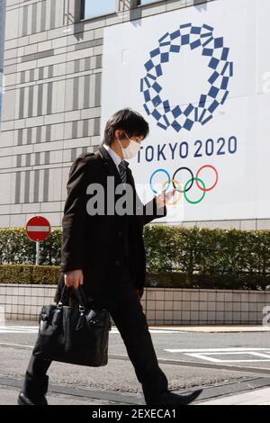 Un piéton portant un masque marche à côté d'une signalisation annonçant les Jeux Olympiques de Tokyo 2020 à Tokyo. Le président du Comité international olympique (CIO), Thomas Bach, a réitéré que le CIO est pleinement engagé à tenir les Jeux de Tokyo cet été. La cérémonie d'ouverture est actuellement prévue pour le 23 juillet. Banque D'Images
