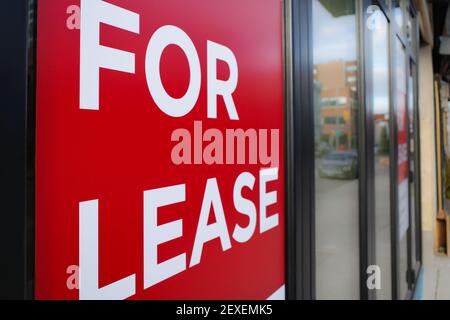 Un panneau « à louer » rouge et blanc est suspendu dans la fenêtre d'une vitrine, avec une scène urbaine floue visible dans les reflets des fenêtres. Banque D'Images