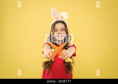 Un petit déjeuner sain. Bon pour vos dents. Grignotez des carottes comme du lièvre. Gamin dans les oreilles de lapin mangeant des carottes. Costume de lapin enfant avec carotte. Nourriture pour petite fille heureuse pour lapins. Enfance saine. Banque D'Images