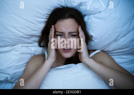 Femme stressée avec mal de tête dormant au lit avec insomnie Banque D'Images