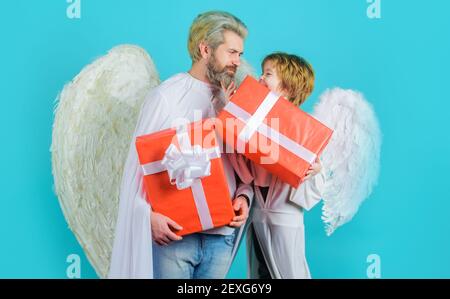 Père heureux avec son fils en costume d'ange avec cadeau. Anges de Saint-Valentin avec boîte cadeau. Le petit garçon de cupidon donne le cadeau de père. Banque D'Images