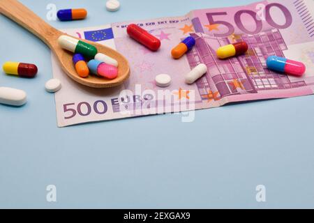 Photographie originale des médicaments sur fond bleu clair, 500 billets en euros et une cuillère en bois Banque D'Images