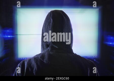 Le pirate anonyme regarde le moniteur de l'ordinateur. Vue de derrière. Banque D'Images