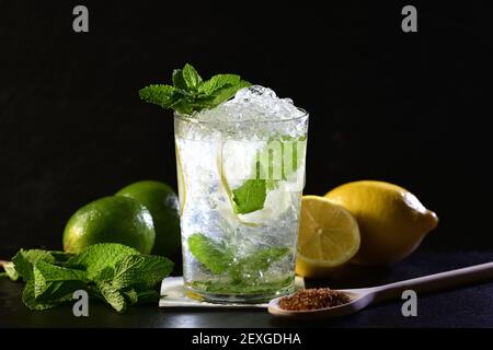 Mise au point sélective et gros plan d'un cocktail mojito avec des feuilles de menthe, des limes, des citrons et une cuillère en bois avec du sucre brun. Concept d'ingrédients frais. Banque D'Images