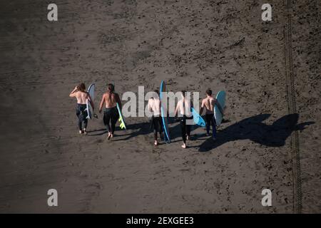 AUCKLAND, NOUVELLE-ZÉLANDE - 21 février 2021 : vue aérienne de cinq surfeurs en combinaisons marchant avec leurs planches de surf sur la plage de Piha Banque D'Images