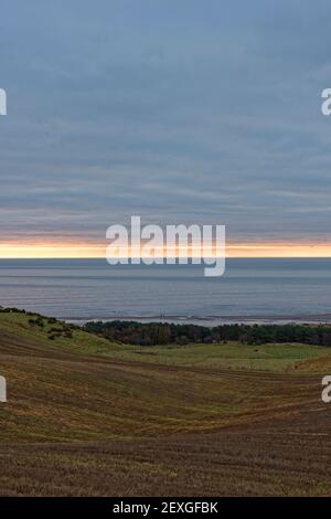 Le soleil se levant sous la couche de Low Cloud au-dessus de la baie de Lunan et les terres agricoles vallonnées derrière la plage, en début de matinée en février. Banque D'Images