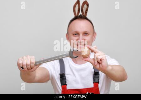 Vacances de Pâques, concept de célébration. Travailleur ou mécanicien souriant drôle porte des oreilles de lapin sur la tête, tenant des clés et peint blanc d'oeuf Banque D'Images