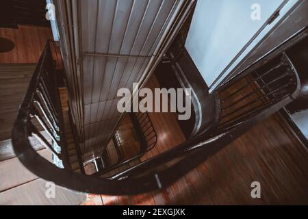 Une vue grand angle depuis le dernier étage d'un ancien entrée du bâtiment d'un escalier en bois incurvé descendant et un arbre d'élévateur à l'intérieur d'un boîtier métallique Banque D'Images