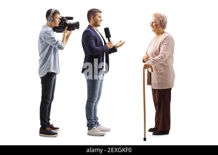 Prise de vue en profil d'un journaliste mâle avec un microphone et un caméraman interviewer une femme âgée isolée sur arrière-plan blanc Banque D'Images