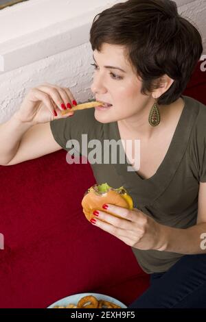 Femme manger Burger frites déjeuner canapé salon repas Banque D'Images