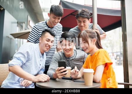 groupe de jeunes adultes asiatiques quatre hommes et un femme regardant le téléphone mobile ensemble à l'extérieur Banque D'Images