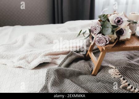 Matin romantique. Table basse en bois avec fleurs sur le lit avec un écossais, une tasse de café, des fleurs et des bougies. Roses lilas avec eucalyptus et anémones. Inter Banque D'Images