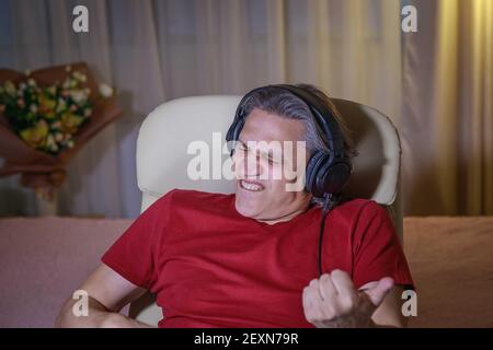 un homme de 50 ans écoute de la musique avec un casque à la maison, assis dans une chaise. Délice relaxant. Banque D'Images