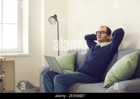 L'homme a pris une pause de travail assis sur un canapé avec un ordinateur portable et de mettre ses mains derrière sa tête. Banque D'Images