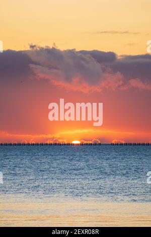 Shoeburyness, Essex. 5 mars 2021 - Sunrise, Thames Estuary, Royaume-Uni - UNE banque de nuages à l'horizon est a partiellement obscurci le soleil lorsqu'il s'est levé au-dessus de l'estuaire de la Tamise, bien qu'elle ait aidé à créer des éclaboussures momentanées de couleurs vives. L'ancien boom de la défense de la Guerre froide est défait par rapport à l'horizon brillant crédit: Timothy Smith/Alay Live News Banque D'Images