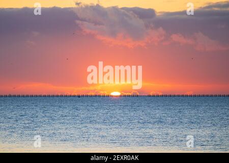 Shoeburyness, Essex. 5 mars 2021 - Sunrise, Thames Estuary, Royaume-Uni - UNE banque de nuages à l'horizon est a partiellement obscurci le soleil lorsqu'il s'est levé au-dessus de l'estuaire de la Tamise, bien qu'elle ait aidé à créer des éclaboussures momentanées de couleurs vives. L'ancien boom de la défense de la Guerre froide est défait par rapport à l'horizon brillant crédit: Timothy Smith/Alay Live News Banque D'Images