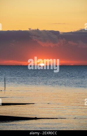 Shoeburyness, Essex. 5 mars 2021 - Sunrise, Thames Estuary, Royaume-Uni - UNE banque de nuages à l'horizon est a partiellement obscurci le soleil lorsqu'il s'est levé au-dessus de l'estuaire de la Tamise, bien qu'elle ait aidé à créer des éclaboussures momentanées de couleurs vives. L'ancien boom de la défense de la Guerre froide est défait par rapport à l'horizon brillant crédit: Timothy Smith/Alay Live News Banque D'Images