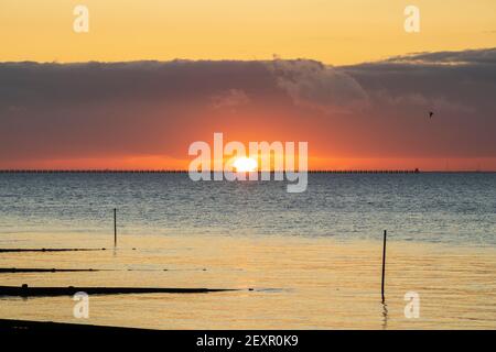 Shoeburyness, Essex. 5 mars 2021 - Sunrise, Thames Estuary, Royaume-Uni - UNE banque de nuages à l'horizon est a partiellement obscurci le soleil lorsqu'il s'est levé au-dessus de l'estuaire de la Tamise, bien qu'elle ait aidé à créer des éclaboussures momentanées de couleurs vives. L'ancien boom de la défense de la Guerre froide est défait par rapport à l'horizon brillant crédit: Timothy Smith/Alay Live News Banque D'Images