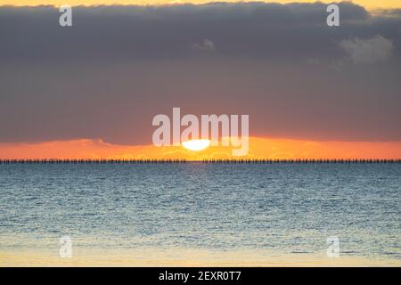 Shoeburyness, Essex. 5 mars 2021 - Sunrise, Thames Estuary, Royaume-Uni - UNE banque de nuages à l'horizon est a partiellement obscurci le soleil lorsqu'il s'est levé au-dessus de l'estuaire de la Tamise, bien qu'elle ait aidé à créer des éclaboussures momentanées de couleurs vives. L'ancien boom de la défense de la Guerre froide est défait par rapport à l'horizon brillant crédit: Timothy Smith/Alay Live News Banque D'Images