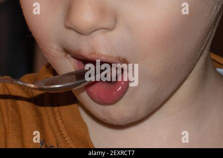 gros plan de la bouche d'un enfant avec des lèvres colorées au chocolat qui est apporter une cuillère à sa bouche Banque D'Images