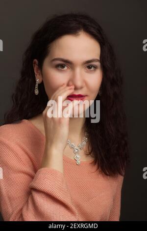 Studio portrait d'une brunette dans une robe pêche, il égratignure son nez avec ses doigts Banque D'Images