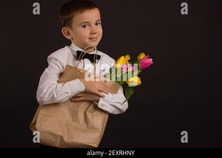 le garçon avec le vitiligo dans une chemise blanche et un Noeud papillon avec tulipes sur fond noir Studio Banque D'Images