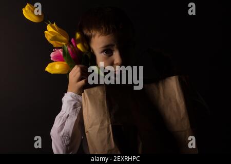 le garçon avec le vitiligo dans une chemise blanche et un Noeud papillon avec tulipes sur fond noir Studio Banque D'Images