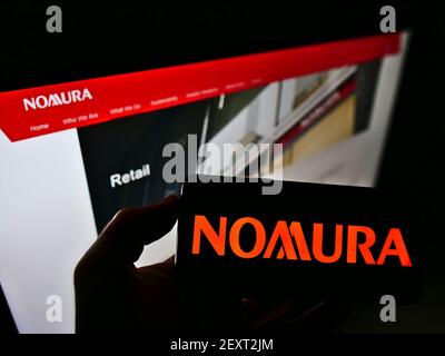 Personne tenant un smartphone avec le logo de la société financière japonaise Nomura Holdings KK à l'écran en face de la page Web d'affaires. Mise au point sur l'affichage du téléphone. Banque D'Images