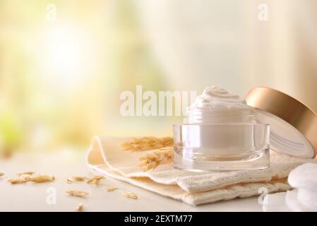 Crème hydratante pour le corps et le visage d'avoine dans un pot en verre avec pointes sur table en bois avec fond de fenêtre Banque D'Images