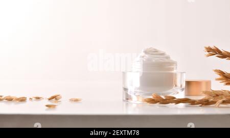 Crème hydratante pour le corps et le visage d'avoine dans un pot en verre avec pointes sur table en bois avec fond blanc isolé Banque D'Images
