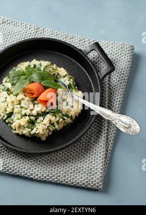 Risotto aux jeunes épinards et saumon fumé servi dans un plateau noir en fonte avec couteau et fourchette Banque D'Images