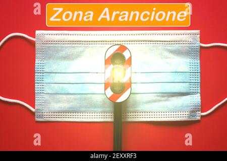 Masque chirurgical avec un feu de circulation avec une lumière jaune, et le texte 'Aranzona cione' se traduisant en zone orange, concept de zone orange pendant Corona Vir Banque D'Images