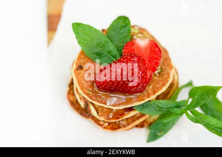 Pile de crêpes dorées avec fraises et branche décorative de menthe. Gros plan Banque D'Images